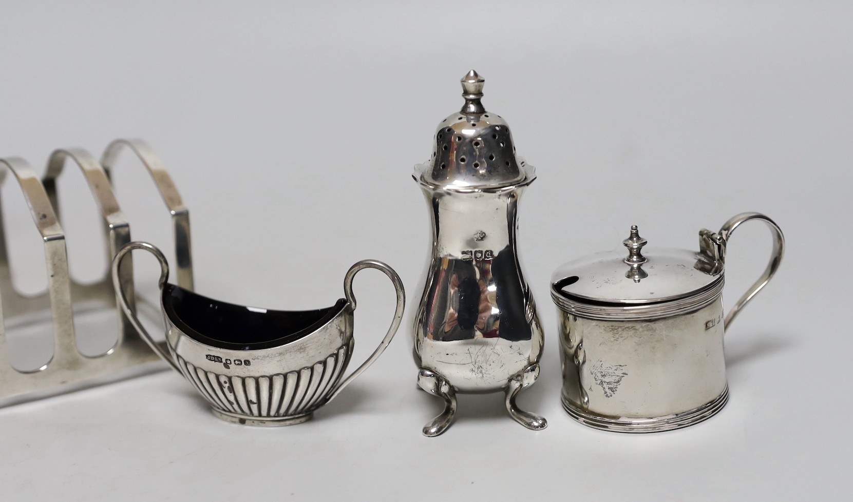 A George V silver seven bar toastrack, Birmingham, 1913, 11.9cm, four silver condiments, a silver mounted glass toilet jar and two silver plated items including a wine funnel.